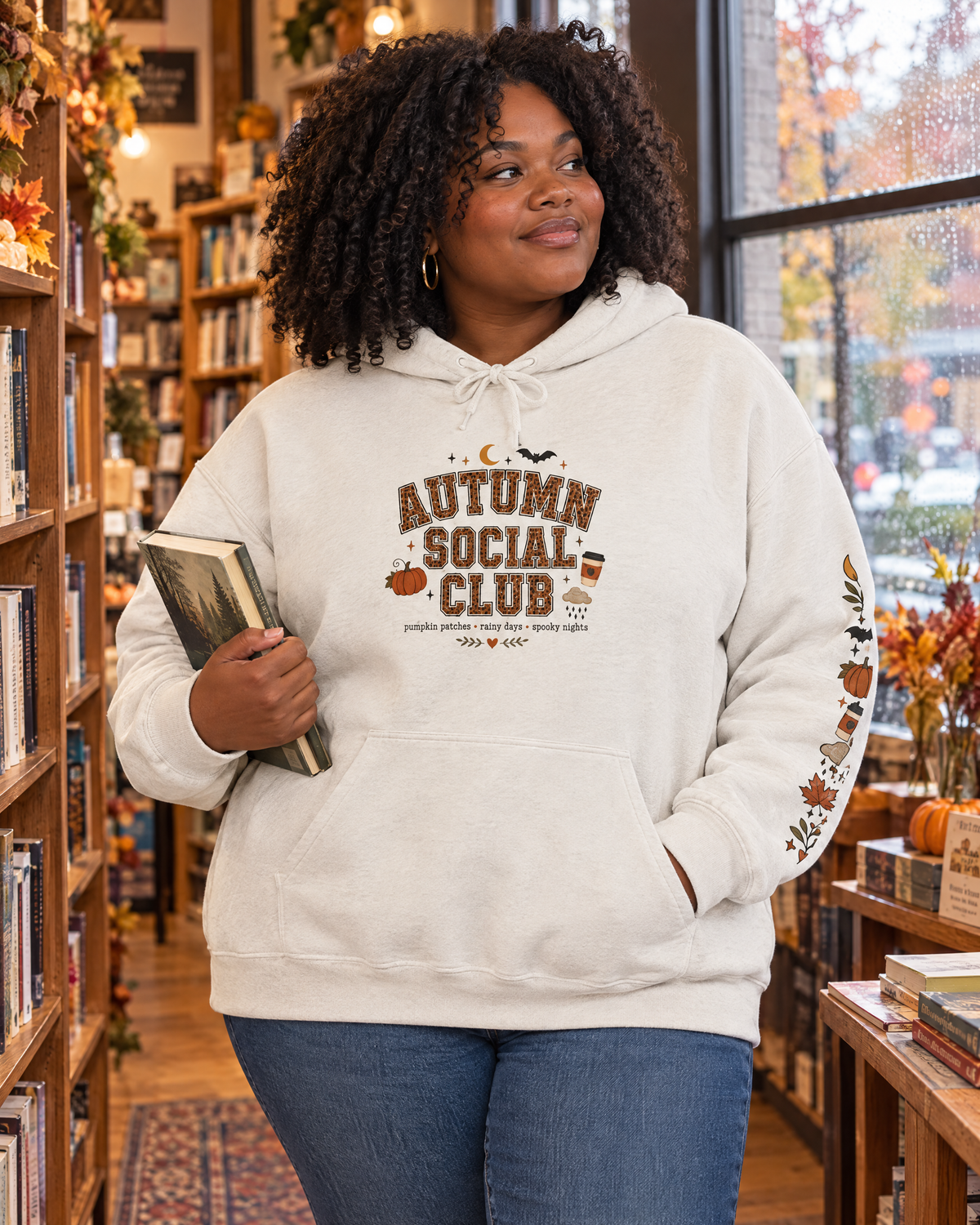 Autumn Social Club hoodie in sand on a plus-size model in a cozy bookstore