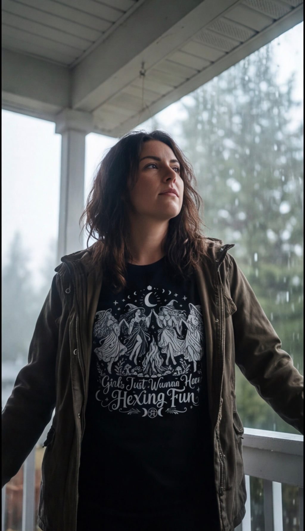 Woman wearing the Girls Just Wanna Have Hexing Fun witch tee with a jacket on a rainy porch.